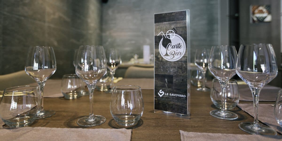 Verres dressés sur une table du Savoyard, la carte du bar posée au milieu
