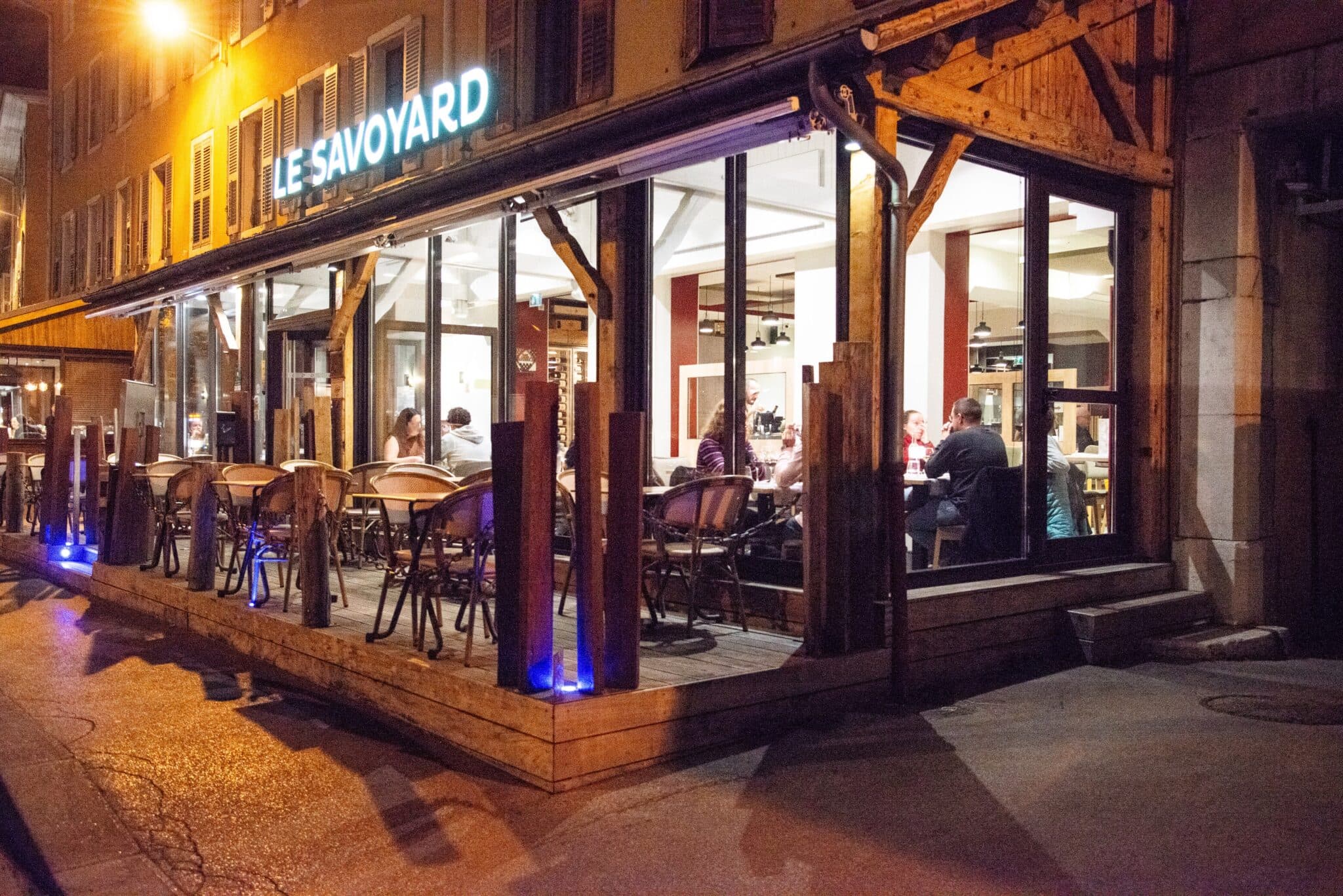 Le Savoyard le soir, l’enseigne allumée au-dessus de la terrasse couverte et de la salle éclairée